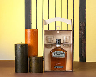 Table Top Setting Showing Large Candles Arranged around a gift Box containing a bottle of Liquor